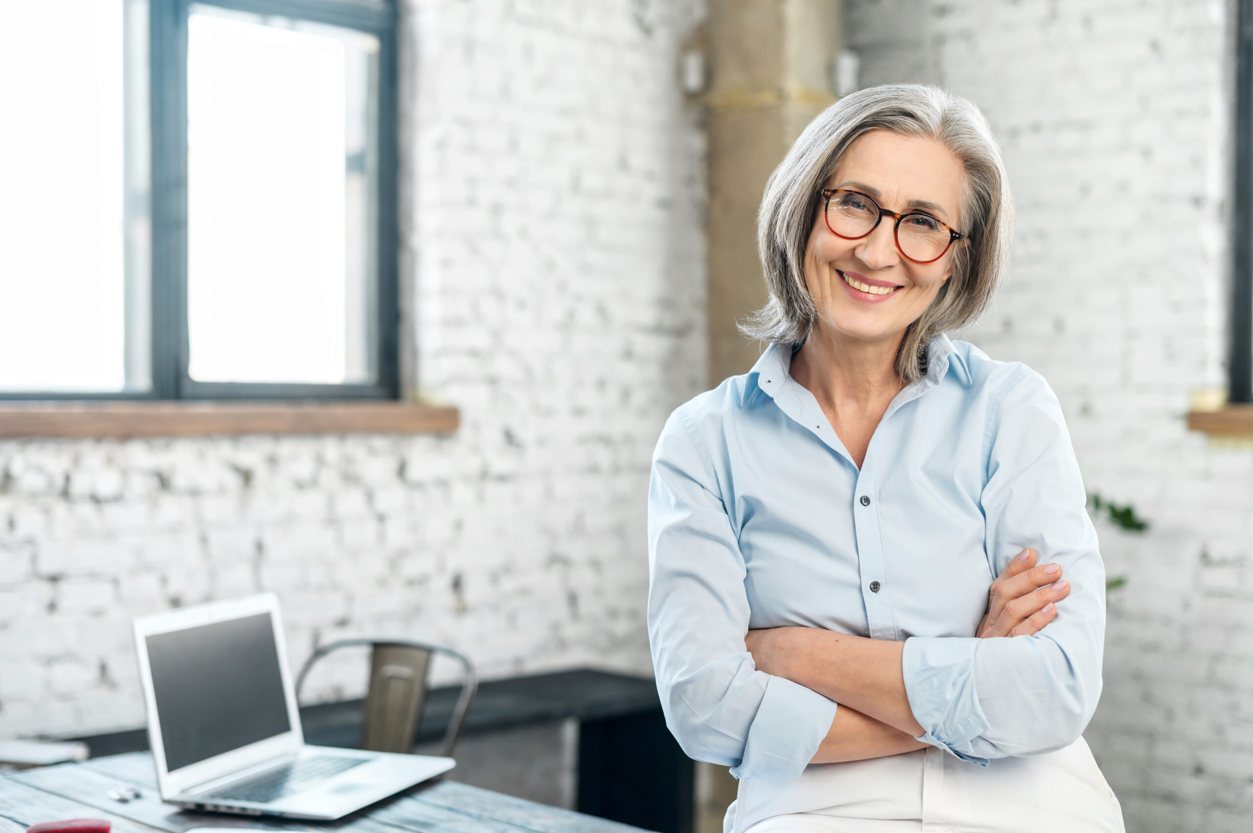 Smiling older woman with folded arms standing in bright office