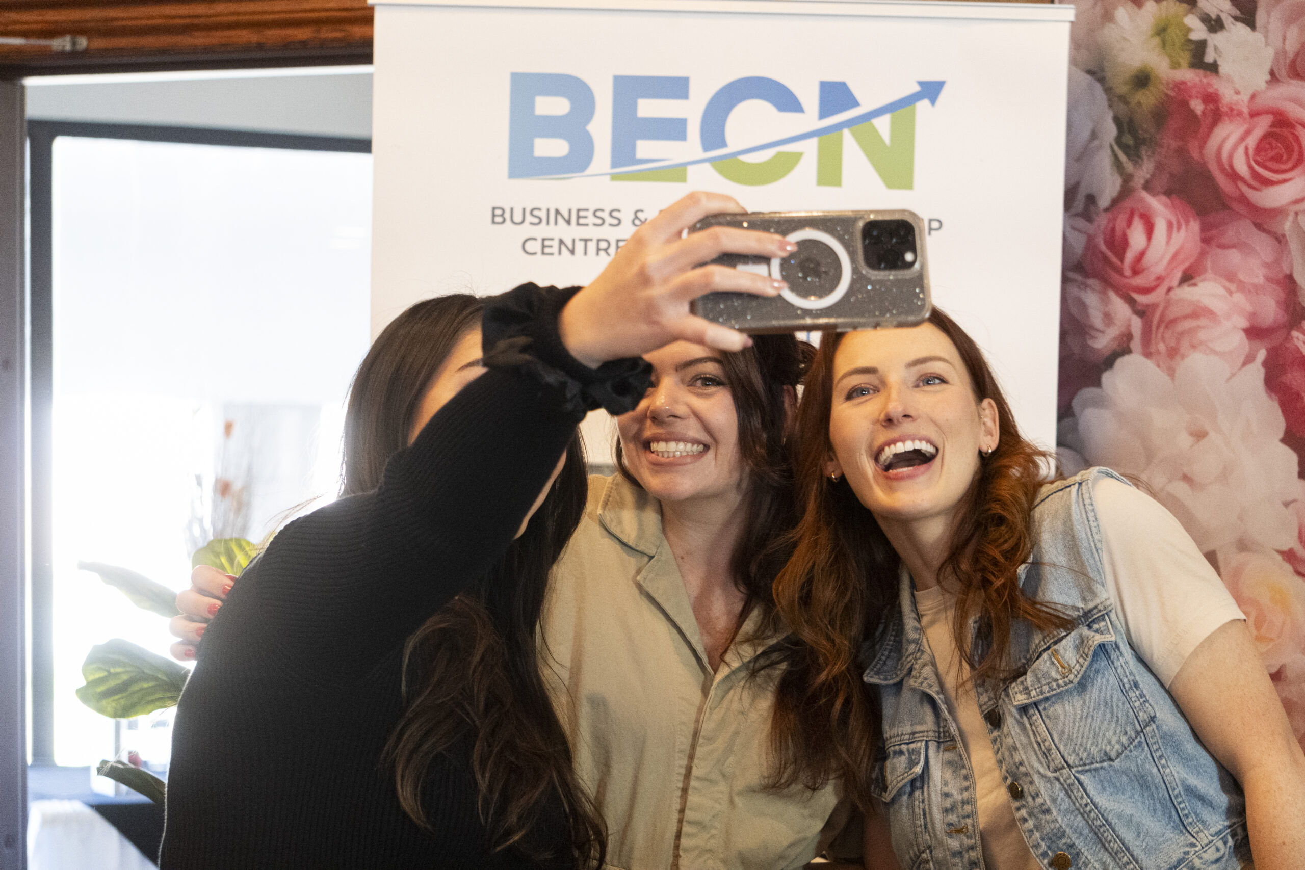 Two women laughing together at She Owns It event with BECN banner behind