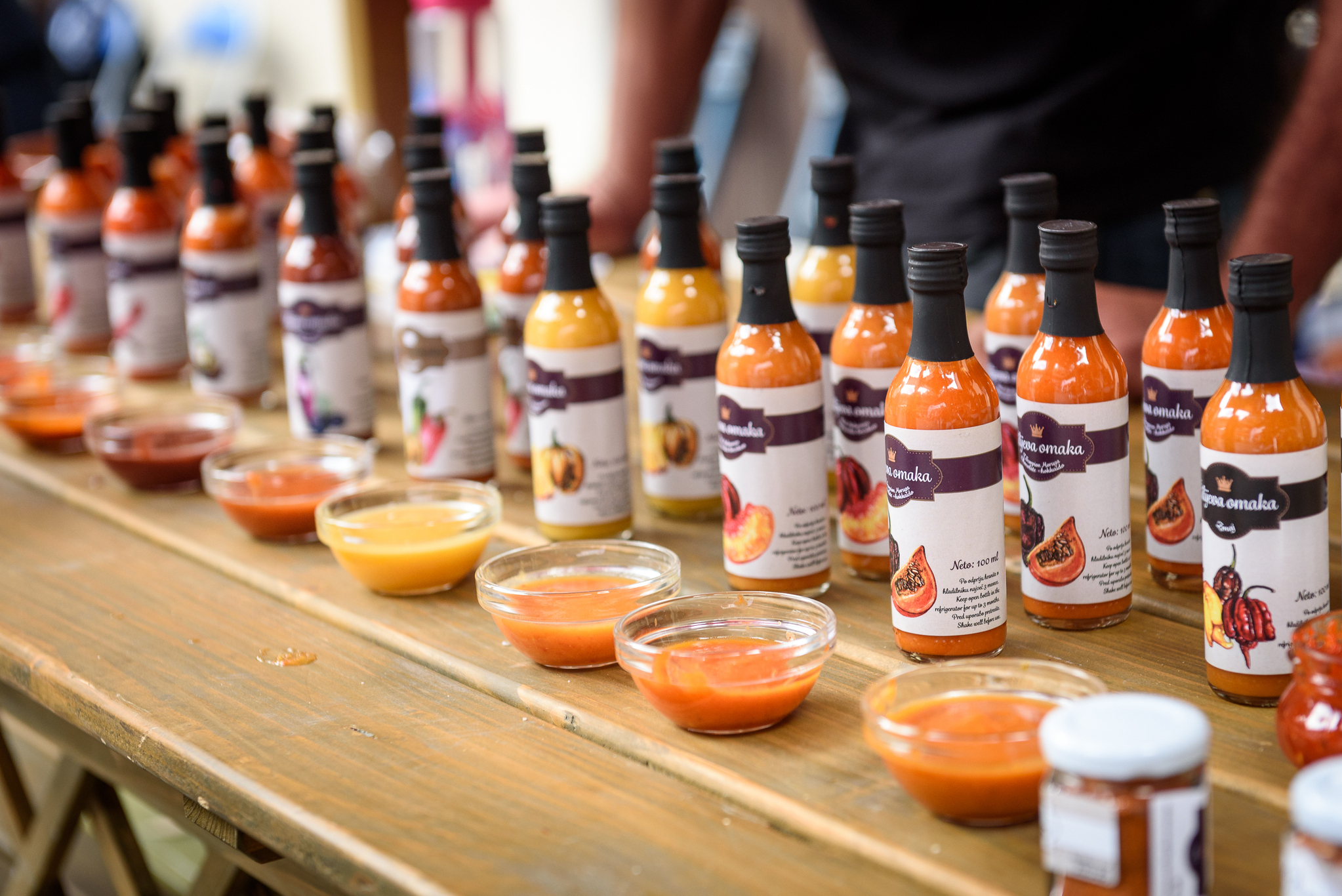 Bottles of a sauce displayed on a table with samples in front of them.